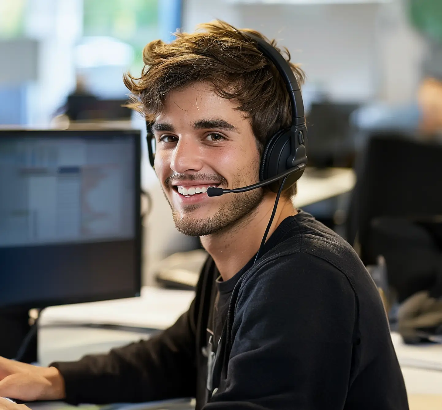 Callcenter-Agent mit Headset im Kundenservice, der vor einem Computer sitzt und lächelt.