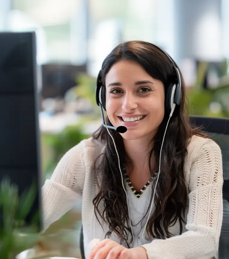 Callcenter-Mitarbeiterin mit Headset, die vor einem Computer sitzt, telefoniert und lächelt.