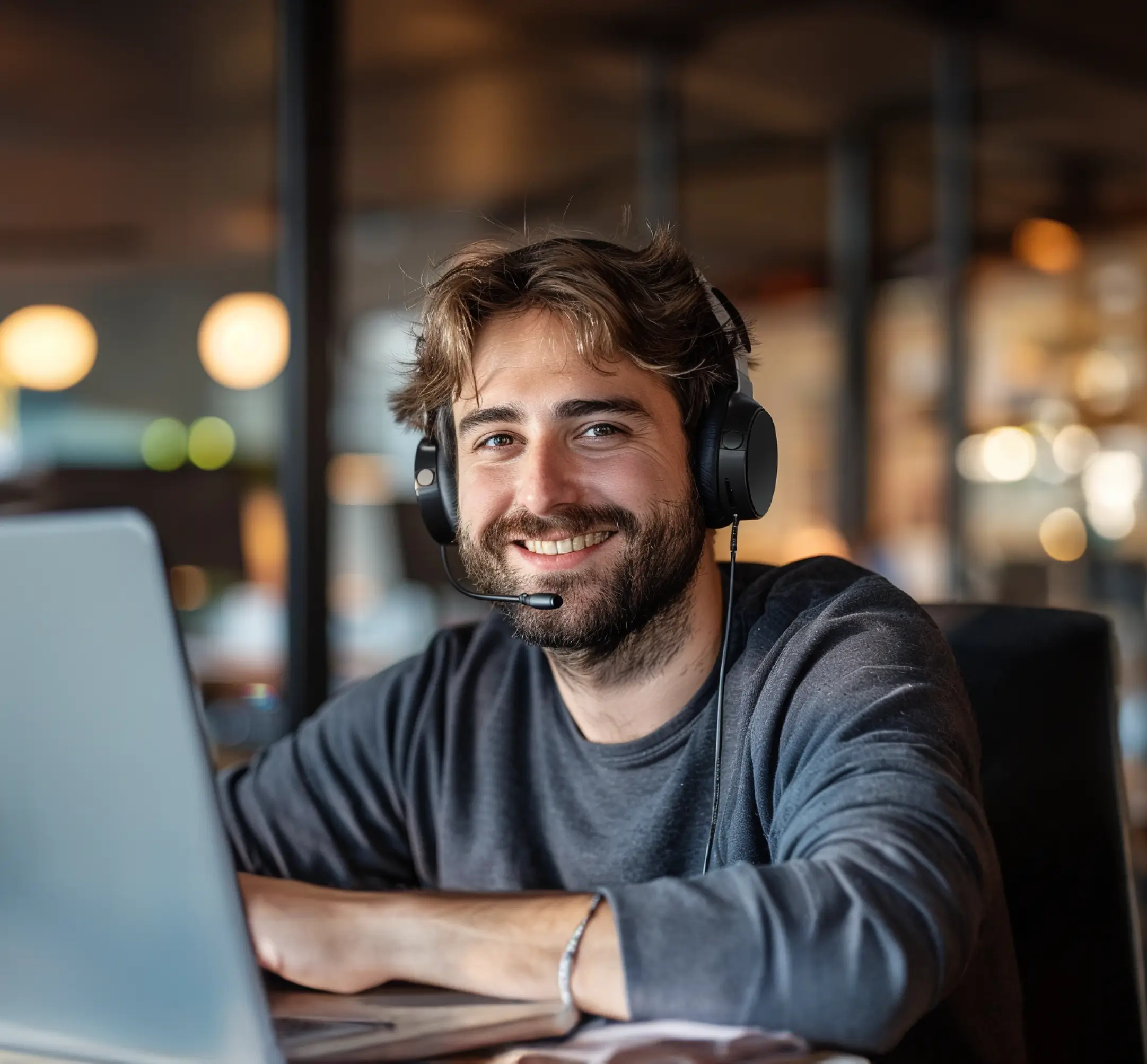 Freundlicher Mitarbeiter mit Headset sitzt vor einem Laptop und lächelt.